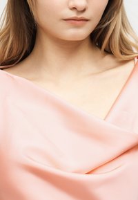 Κοντινό πλάνο μιας γυναίκας που φοράει ανοιχτό ροζ σατέν τοπ με ακάλυπτους ώμους, δείχνοντας το λαιμό της, τις κλείδες και μέρος των χειλιών της.