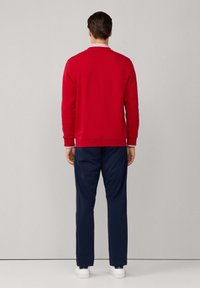 Felpa rossa con polsini e colletto a coste, abbinata a pantaloni blu navy. L'outfit è completato da sneakers bianche. Visto da dietro.