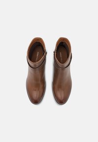 Bottes cheville en cuir marron à finition lisse, bout arrondi, fermeture éclair latérale et bande élastique subtile autour de la cheville.