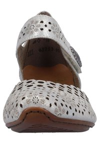 Zapato de piel metálica blanca con patrones florales recortados, correa ajustable y suela marrón. Punta redondeada y diseño de perfil bajo.