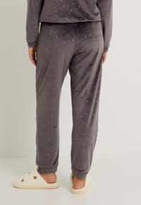 Pantalon de lounge gris en tissu doux, avec un motif d'étoile et de croissant de lune. Poignets aux chevilles et coupe décontractée.