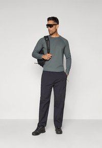 Halli pika varrukaga tekstuuriga top, mustad taskupüksid, mustad tossud ja päikeseprillid; modell kannab musta seljakotti polsterdatud rihmadega.