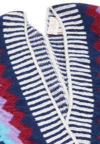 Coperta lavorata a maglia con motivi a zigzag nei toni blu navy, rosso e azzurro chiaro, con strisce bianche lungo il bordo e una finitura morbida e testurizzata.