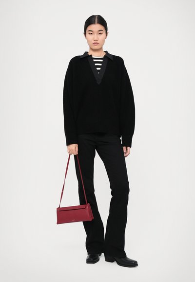 Oversized black knitted sweater with a deep V-neck, layered over a striped top. Black flared pants and a red crossbody bag complete the outfit.