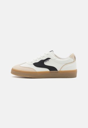 Alacsony szárú sportcipők, fehér szintetikus bőrből, fekete és bézs kiegészítőkkel, gumitalppal és struktúrált orrésszel.