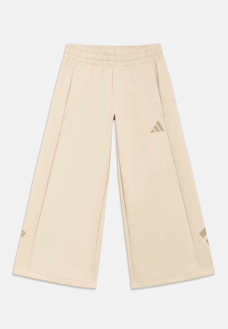Beige bukser med vide ben, elastisk taljebånd, sidelommer og diskrete Adidas-logoer i matcherende farve på underbenene.