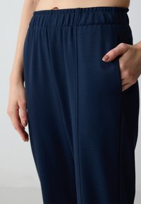 Marineblauwe sportbroek met een zachte textuur, voorzien van een elastische tailleband en zijzakken. Gedetailleerde stiksel langs de naden.