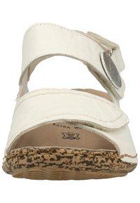 White leather sandal featuring two adjustable straps, a circular metallic accent, and a textured tan rubber sole with speckled detailing.