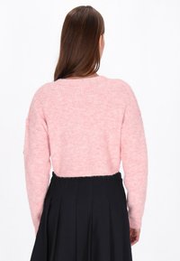 Pasažinė šviesiai rožinė trumpa megztinis su raukšlėta tekstūra, ilgomis rankovėmis ir apvaliu iškirpimu, derinama su juoda raukšlėta suknele.