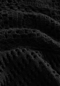 Tessuto a maglia nero scuro con un motivo a nido d'ape e una superficie morbida e pelosa, in vista ravvicinata.
