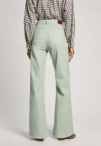 Light green flared jeans made from soft fabric, featuring two back pockets and a brown leather patch on the waistband.