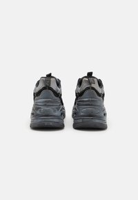 Black sneakers with textured fabric, smooth rubber soles, and reinforced heels. Features branding on the back and contrasting material accents.