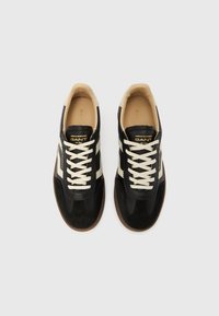 Schwarze und cremefarbene Sportsneaker mit Schnürung vorne, aus Wildleder und Leder, hellen Schnürsenkeln und brauner Gummisohle.