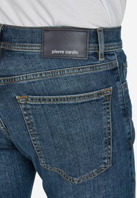 Dunkelblaue Denim-Jeans mit einem Lederetikett mit der Aufschrift "Pierre Cardin" am Bund, featuring kontrastierenden Nähten und klassischem Taschendesign.