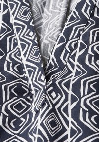 Navy blå stofbluse med et geometrisk hvidt mønster med varierende former. V-hals med ren syning og blød struktur.