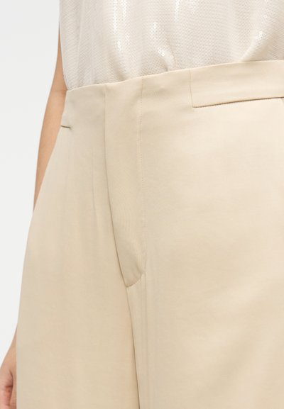 Bordinės plačios kelnės su lygiu paviršiumi, priekyje kišenės ir vidutinio aukščio liemuo. Kelnės parodytos su šviesios spalvos viršutine dalimi.