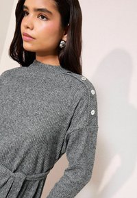 Abito grigio a coste con colletto alto, bottoni laterali e vita cintrata. Il tessuto ha una consistenza morbida e una vestibilità comoda.