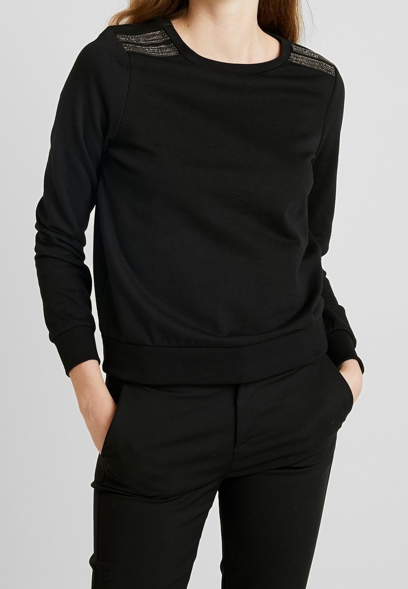Sweat-shirt noir en tissu doux, avec un col rond, des manches longues et des accents texturés sur les épaules.