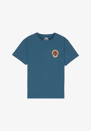 Bawełniany turkusowy t-shirt z okrągłym logo, zestawiony z niebieskimi szortami dżinsowymi o długości do kolan z postrzępionym wykończeniem. Obuwie to ciemne trampki.