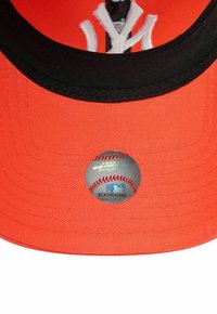 Casquette orange avec une visière noire, comportant un logo brodé blanc. Dispose d'un autocollant circulaire de la MLB avec un graphique de baseball sur le dessous.