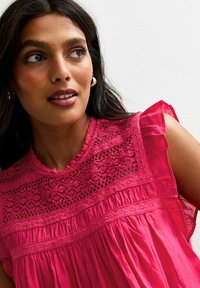 Korte mouwen, roze blouse met kantdetails bij de halslijn, geplooide textuur en volants aan de mouwen. Glad stof en scalloped halslijn.