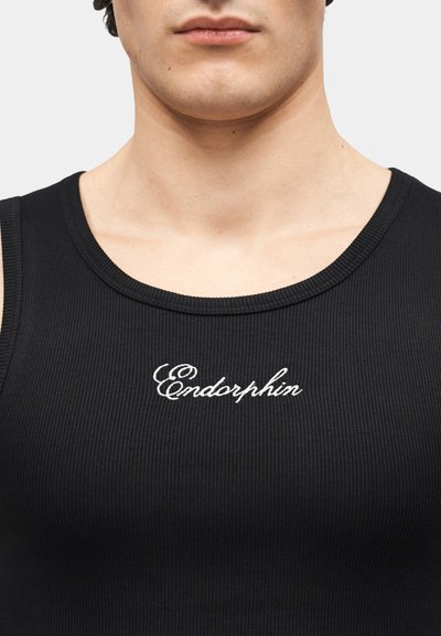 Gros plan d'une personne portant un débardeur côtelé noir avec le mot "Endorphin" brodé en blanc sur la poitrine.
