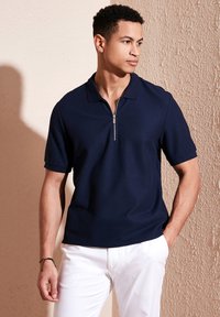 Polo de marină cu mâneci scurte, guler cu fermoar și un material texturat. Asortat cu pantaloni albi. Design simplu, fără modele.