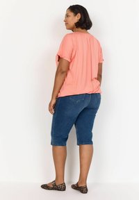 Korallfärgad kortärmad topp i kombination med mörkblå knälånga jeansshorts. Utsmyckad med en sidoklyfta, bärs med leopardmönstrade ballerinas.