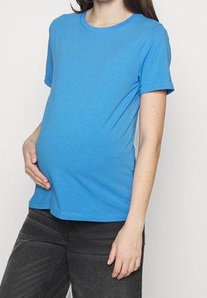 Sininen lyhythihainen t-paita pehmeää kangasta, jossa on pyöreä kaula-aukko ja rento malli, päällä raskaana olevan vatsa. Näkyvät harmaat housut.