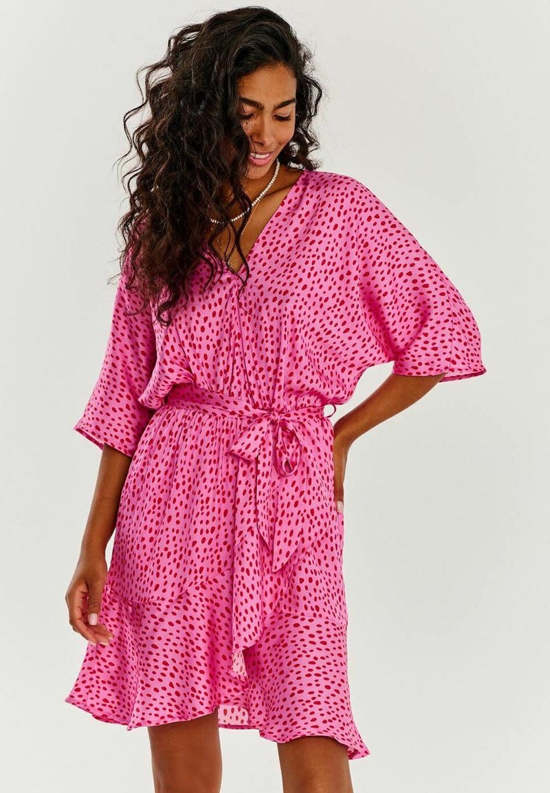 Růžové šaty volného střihu s výstřihem do V, krátkými rukávy a zavazovacími pásky. Tkanina má puntíkovaný vzor v tmavších odstínech růžové.