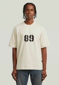 Crème-kleurige katoenen t-shirt met korte mouwen, voorzien van een grote zwarte "89" grafiek op de voorkant, rechte zoom en een relaxte pasvorm.