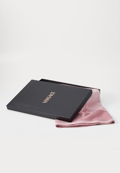 Boîte rectangulaire noire avec le logo doré "VERSACE", partiellement ouverte, révélant un foulard rose clair avec un motif subtil et une texture douce.