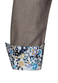 Tessuto di pantaloni marrone con un polsino a motivo floreale che presenta fiori blu, bianchi e marroni su uno sfondo chiaro. I bordi del polsino sono rifiniti con cura.