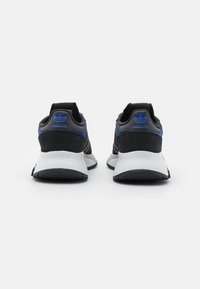 Svarta och grå sportskor med en texturerad ovandel, blåa detaljer, en vit mellansula och en svart gummiyttersula; bakifrån visad.