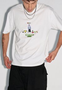 Biała bawełniana koszulka z krótkim rękawem, z luźnym krojem, zdobiona projektem w stylu pixel art, przedstawiającym postać, trofea i różne przedmioty.