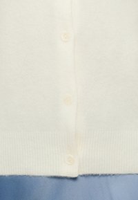 Λευκό κασμιρένιο ζακέτα με ριμπ τελείωμα, που διαθέτει έξι στρογγυλά λευκά κουμπιά κατά μήκος εμπρός. Μαλακό, υφασμένο ύφασμα.