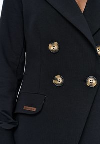 Zwarte dubbelgeknoopte blazer van soepel materiaal, met goudkleurige knopen en een opgestikte zak met een merklabel.