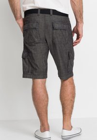 Pantaloni cargo grigi scuri in tessuto testurizzato, con diverse tasche a toppa e una cintura elastica nera. Indossati con sneakers bianche.