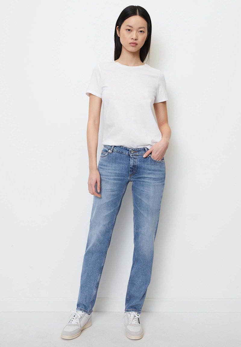 Weißes T-Shirt mit kurzen Ärmeln, kombiniert mit hellblauen, geraden Jeans, die ein klassisches Fünf-Tasche-Design und eine leichte Ausbleichung aufweisen.