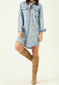 Denimklänning i ljusblått, med långa ärmar, två bröstfickor och knappstängning fram. Bärs med tanfärgade stövlar i mocka som går upp till knäna.