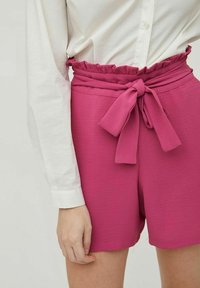 Fuchsiové šortky s volánkovým elastickým pasem a mašlí, vyrobené z texturované látky. Spárované s bílou košilí na knoflíky.