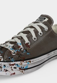 Καφέ Converse sneaker χαμηλού τύπου με λευκά κορδόνια και σόλα, με πολύχρωμες πιτσιλιές μπογιάς στην περιοχή των δακτύλων και στα πλευρά.