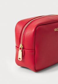 Red cosmetic bag with a rectangular shape, smooth faux leather material, gold zipper, and "VALENTINO" logo embossed on the side.