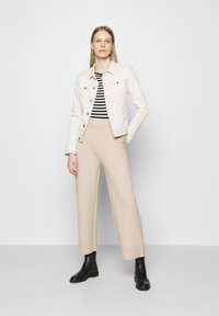 Giubbotto di denim beige chiaro sopra una maglietta a righe bianche e nere, abbinato a pantaloni beige a gamba larga e stivaletti neri.