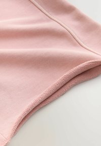Tissu tricoté rose doux avec des coutures visibles et un bord plié, montrant la texture et les détails de la couture.