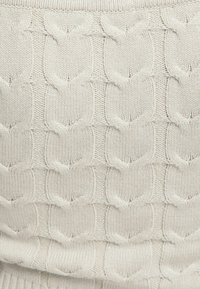 Light beige knitted sweater featuring a textured cable pattern with raised elements. Soft fabric with a smooth finish.