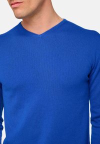 Pull en tricot bleu avec un col en V. Le tissu semble lisse et légèrement texturé, s'ajustant étroitement autour du cou et des épaules.