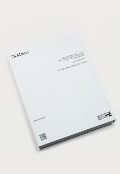 Λευκό κλειστό βιβλίο με τίτλο "DI Milano" με κείμενο για τον μονοχρωματικό μινιμαλισμό, βαθιά έρευνα και έναν κωδικό QR σε απλό φόντο.