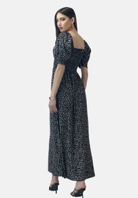 Robe maxi noire à motifs floraux avec des manches bouffantes, un décolleté carré et une taille cintrée. Elle présente une jupe fluide avec de petits motifs blancs.