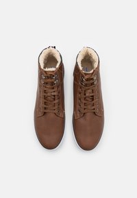 Brune skinn høye sko med faux pels fôr, rund tå og metalløyer. Har brune snører og en hvit gummisåle.